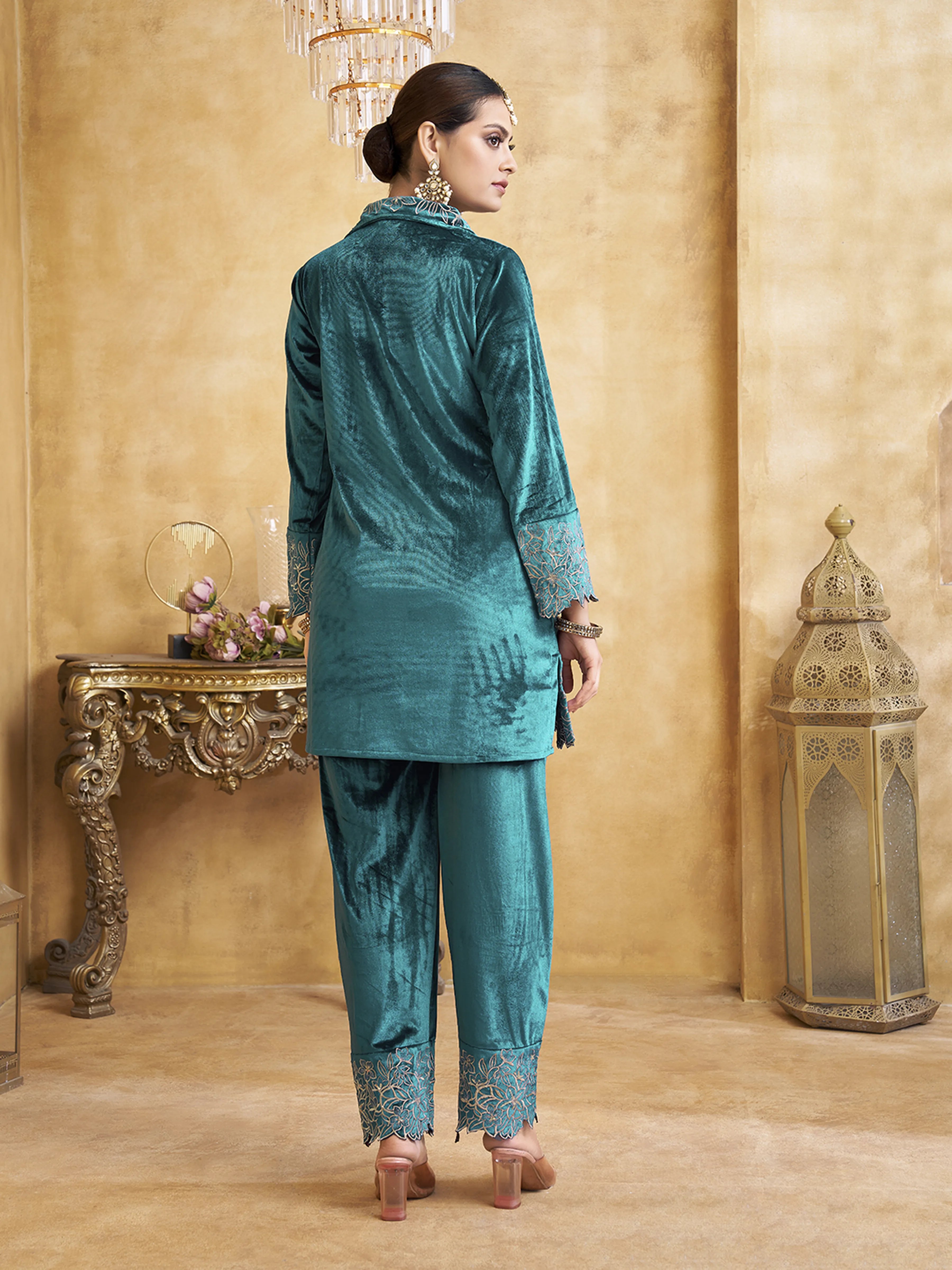 Woman in teal traditional outfit standing in a decorated room with gold accents.